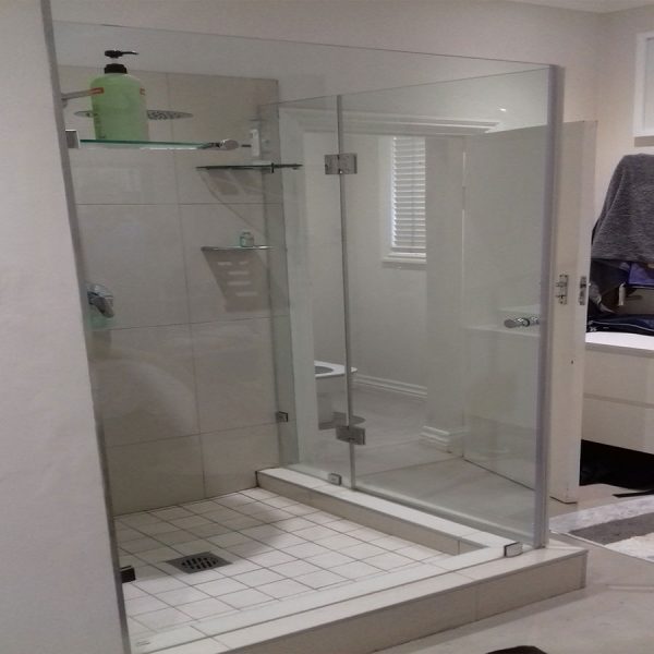 Frameless shower enclosure with door hinging off a panel